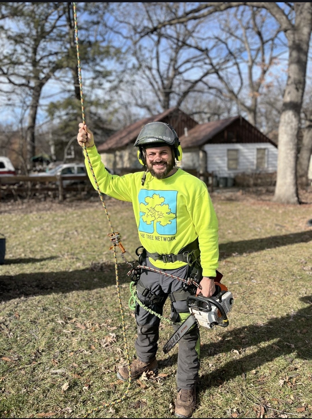Professional tree service technician with full safety equipment cutting trees in Ankeny Iowa